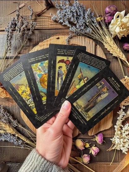 Hand holding tarot cards on a wooden surface with dried flowers and herbs.