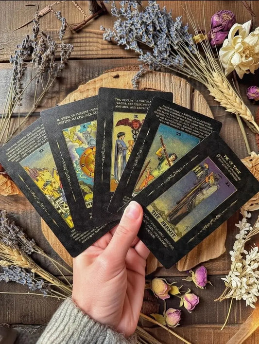 Hand holding tarot cards on a wooden surface with dried flowers and herbs.