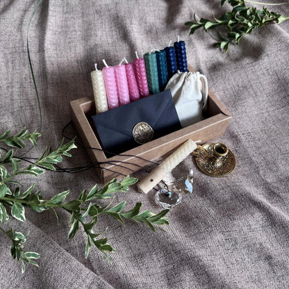 Set of colorful candles from natural beeswax  in a wooden box with decorative elements on a textured fabric background