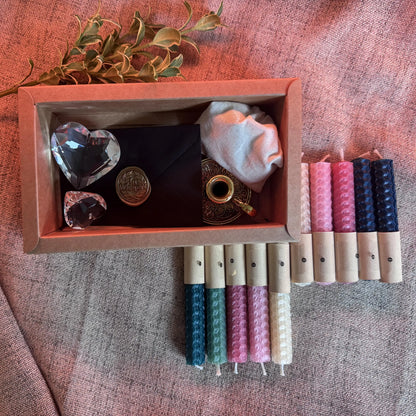 Set of natural beeswax candles with decorative items in a wooden box on a textured fabric background