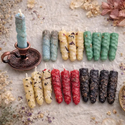 Assorted natural beeswax candles of different colors and textures on a textured surface with dried flowers.