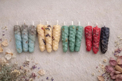 Row of colorful  natural beeswax candles on a textured surface with dried flowers and herbs.