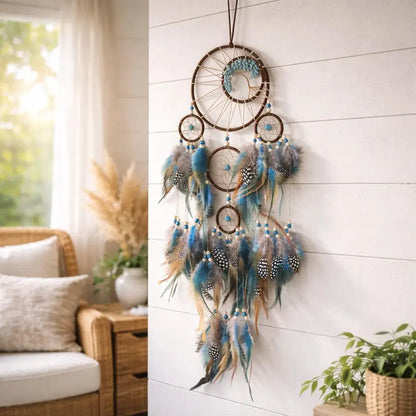 A bohemian dreamcatcher wall hanging with multiple brown wooden rings, blue and teal feathers, and patterned beads, displayed on a white shiplap wall in a bright, modern room.