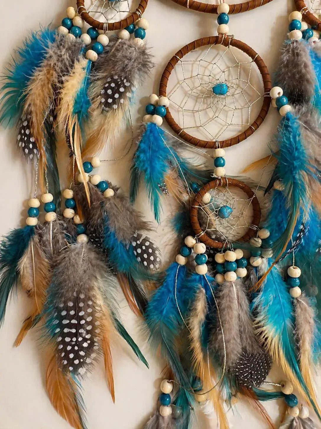 Bohemian dreamcatcher wall hanging with three woven brown hoops, turquoise beads, white and tan beads, and feathers in turquoise, gray, brown, and tan.