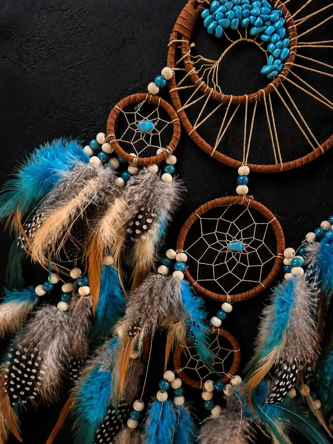 A set of three dreamcatchers with brown wrapped hoops, beige webbing, turquoise beads, and blue, gray, and brown feathers, arranged against a dark textured background.