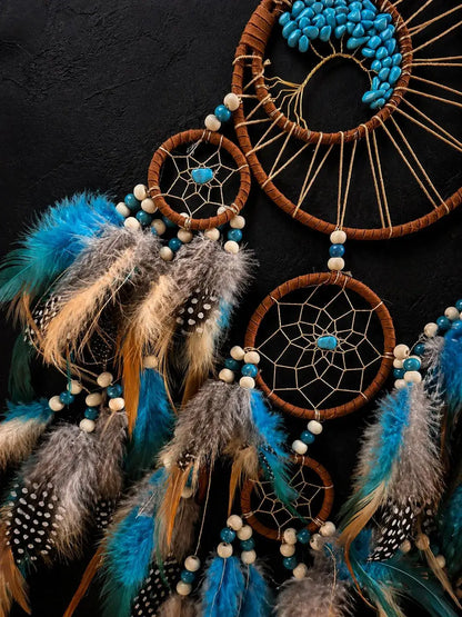 A set of three dreamcatchers with brown wrapped hoops, beige webbing, turquoise beads, and blue, gray, and brown feathers, arranged against a dark textured background.