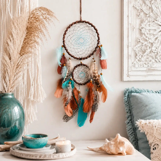 Decorative dreamcatcher with feathers hanging on a wall with a vase, bowl, and shell in the foreground.